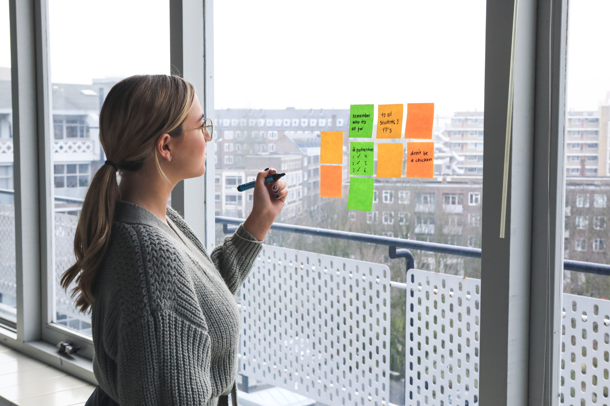 A woman strategizing with sticky notes on a window, representing the long-term planning and structured approach of strengths-based coaching for sustained personal and professional growth.