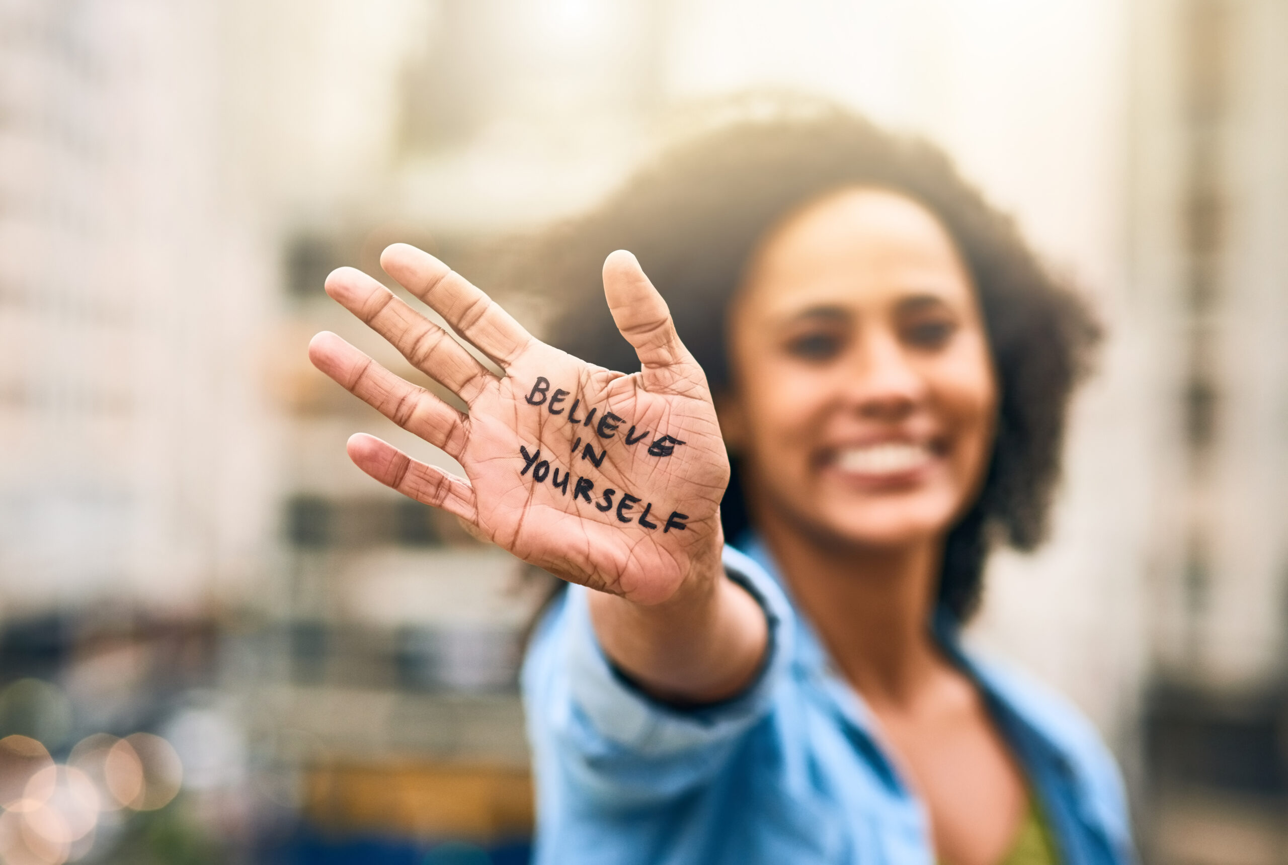 A confident woman proudly displays "Believe in Yourself" on her hand, symbolizing the power of embracing unique talents to achieve goals and live with purpose.